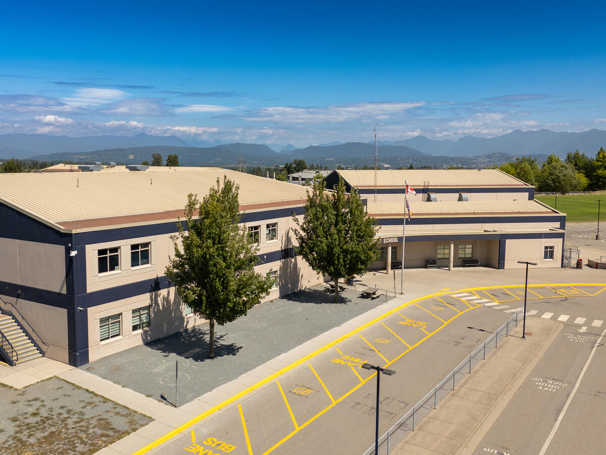 Exterior image of a middle school. Blue sky, clouds and mountains in the back of image behind the school.