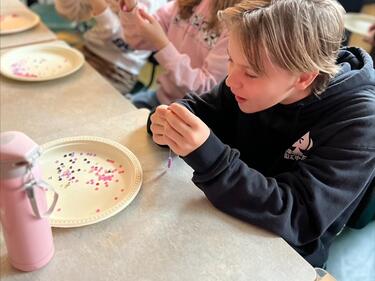 Three students sitting at a table, focused on threading beads