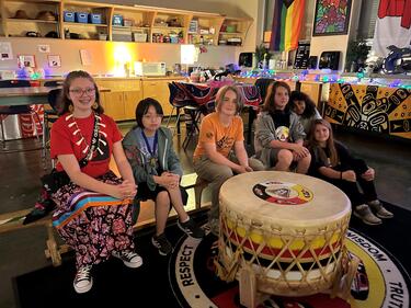 Indigenous Students sitting on a bench in front of a large drum