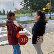 Two adults talking outside, one is holding stop sign.